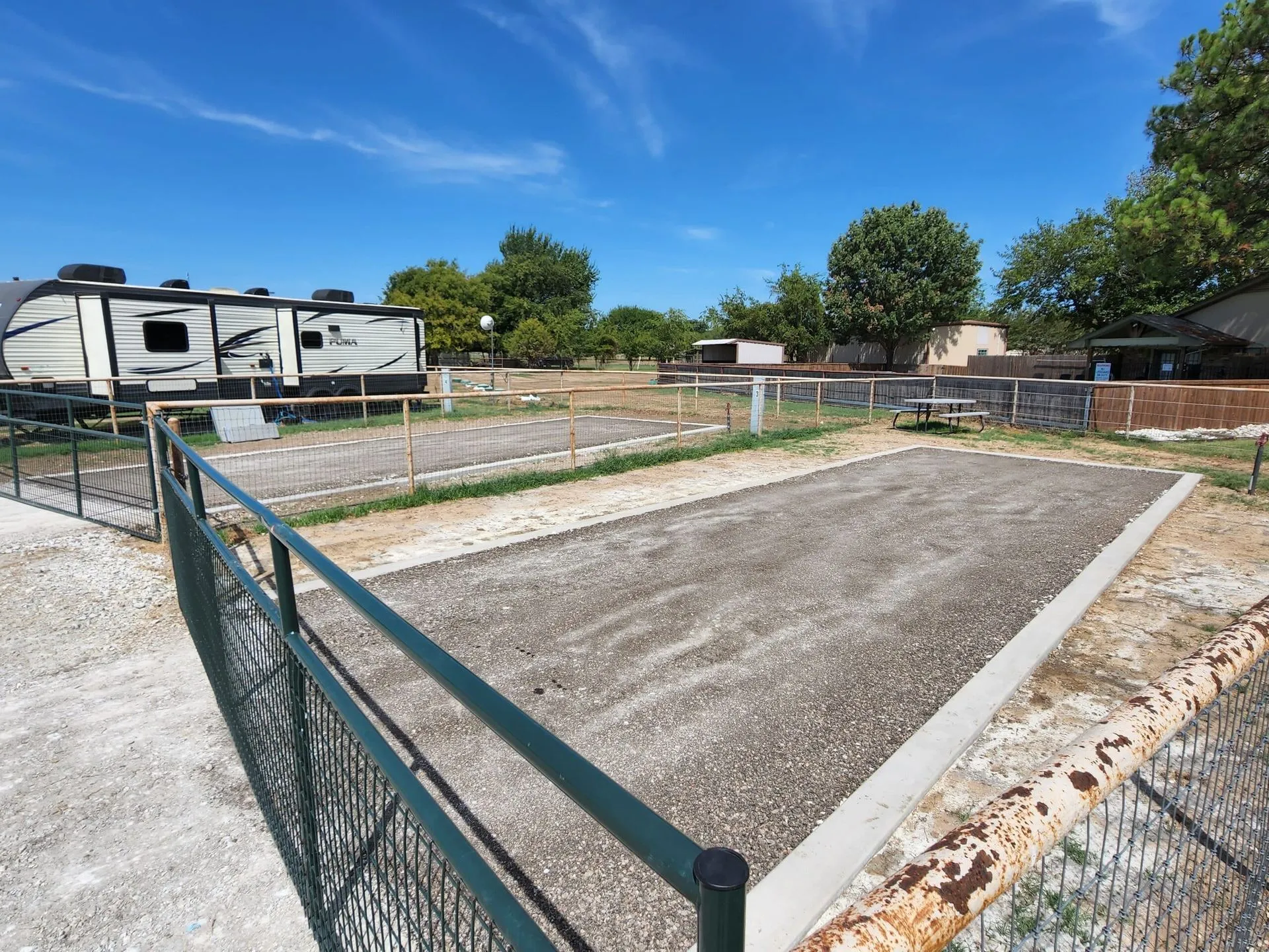 An empty fenced RV site with green gate and concrete pads, ready for arrival, at Waggin' Tail Ranch RV Resort in Pilot Point, TX